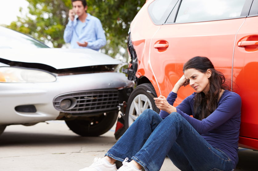 Woman leaned up against her car after wreck while the other driver calls to make an insurance claim